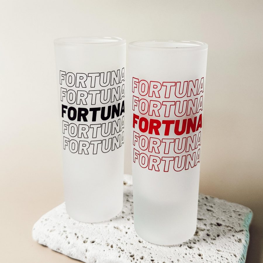 Zwei matte Shotgläser mit dem FORTUNA Schriftzug im Repeat-Design, in Schwarz und Rot, dekorativ arrangiert auf heller Steinfläche.